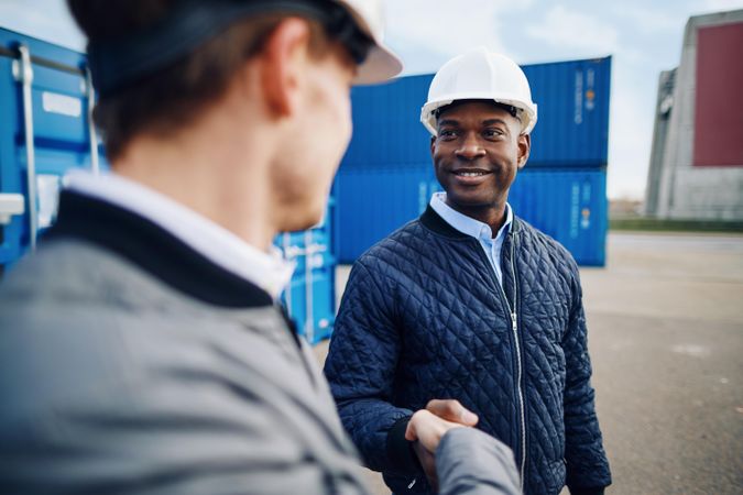 Two men in hard hats smiling on a building site shaking hands