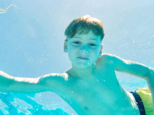 Funny boy swimming underwater looking at camera