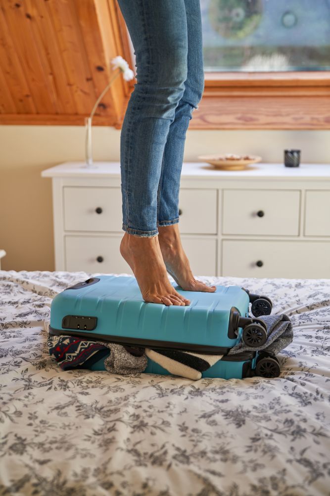 Crop person packing suitcase in bedroom