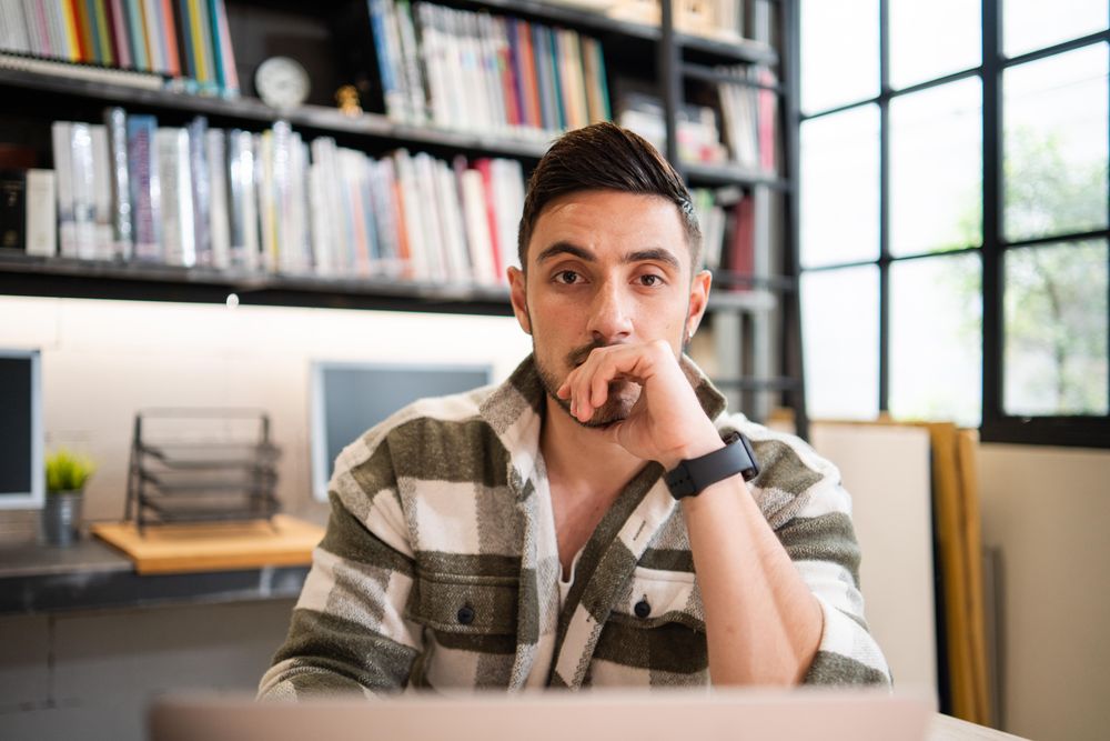 Male creative looking at camera above laptop in relaxed modern office