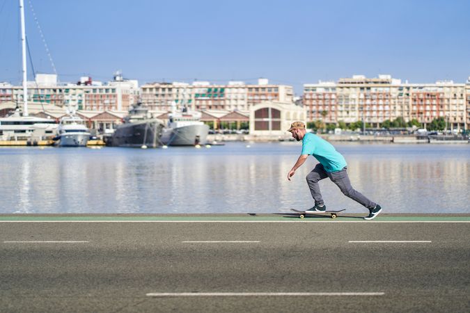 young man riding a skateboard on a road next to the port in the morning
