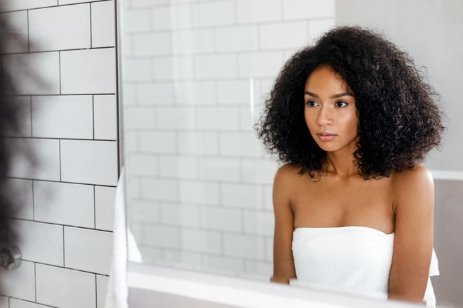 Serious Black woman with curly hair looking in the mirror