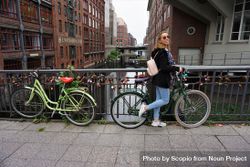 Young woman standing beside a bicycle parked on sidewalk in Hamburg, Germany 4mBezb