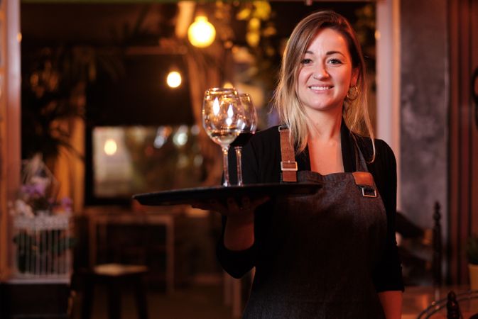 Cheerful waitress holding tray with wineglasses