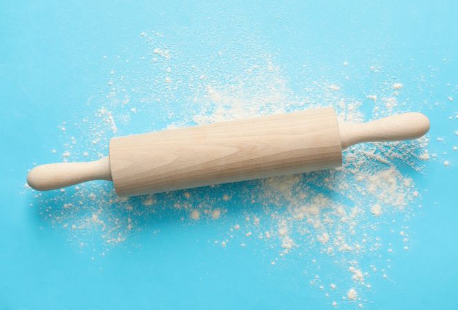 Rolling pin and flour on blue background