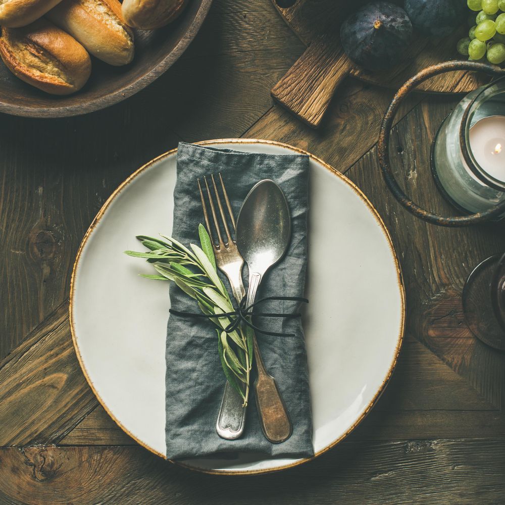 Top view of fall holiday table decoration setting, with grapes, bread, and candle, square crop