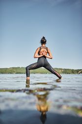 Rear view of young woman doing reverse prayer yoga pose in shallow lake water