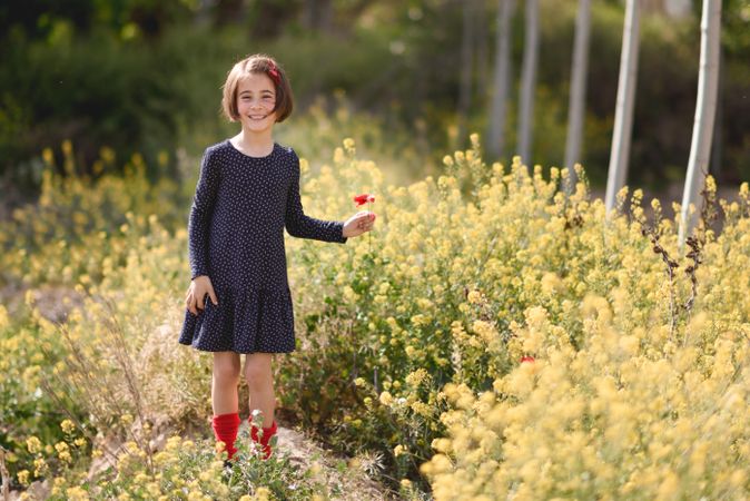 Child with a red flower in a beautiful field surrounded by yellow flowers