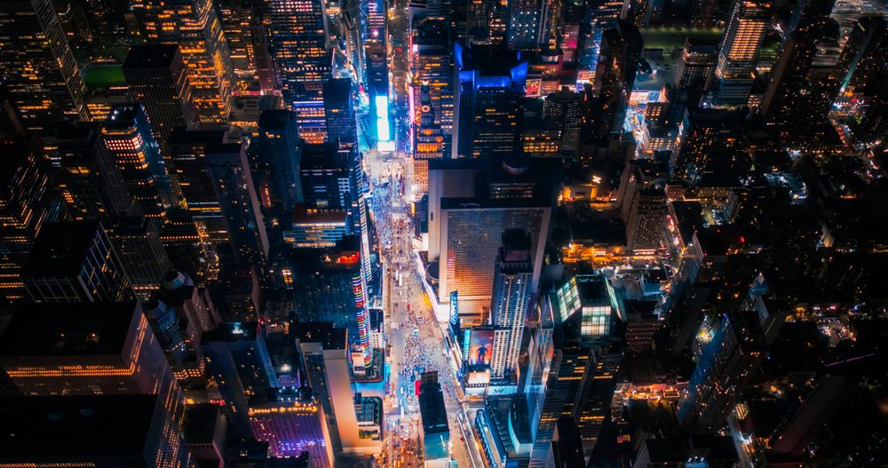 Night Aerial Photo of New York City with Skyscraper Spires and Straight Busy Streets with Cars and Yellow Taxi Vehicles. Lowered Helicopter View of Office Buildings in a Big Urban Center