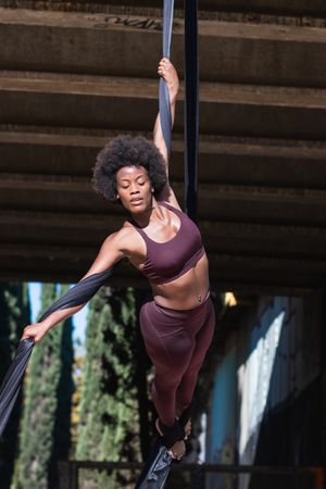 Slim woman doing yoga with aerial silks in city