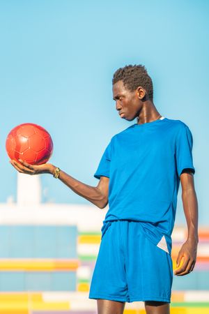 Black teenager with football ball against sky