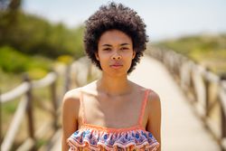 Portrait of woman with afro hair standing on wooden footpath by the coast