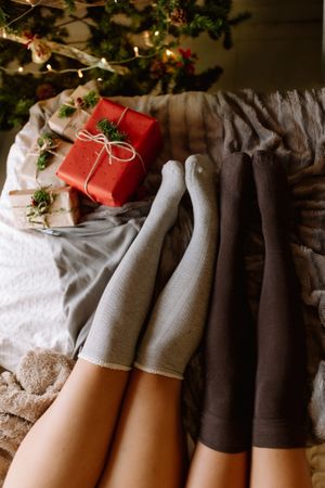 Two friends with knee high socks in winter holidays at home near christmas tree in cozy interior with christmas presents.
