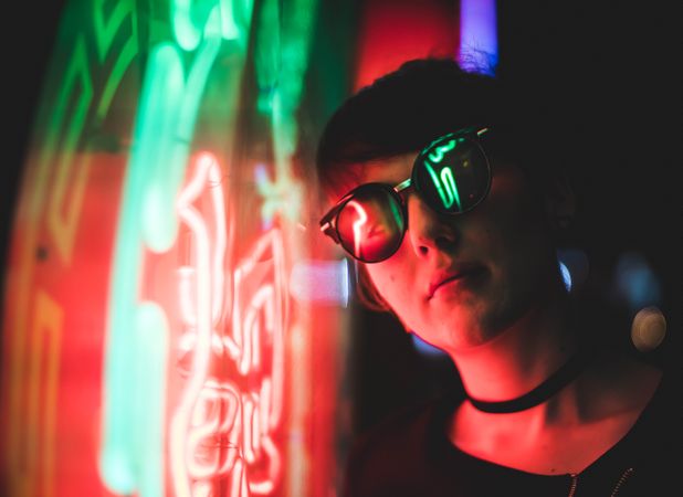 Woman wearing sunglasses standing by the colorful neon light
