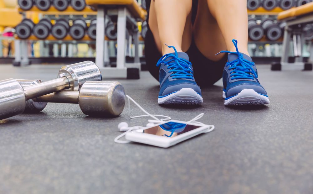 Person sitting next to phone and silver weights in gym