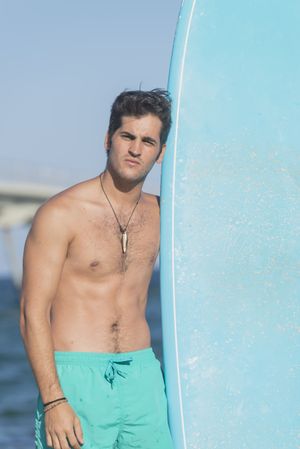 Front of shirtless male surfer standing with blue board on the coast