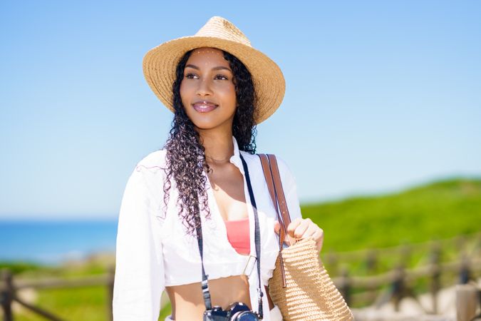 A Young Woman Embracing Summer Fashion at the Beach While Holding a Camera and Smiling