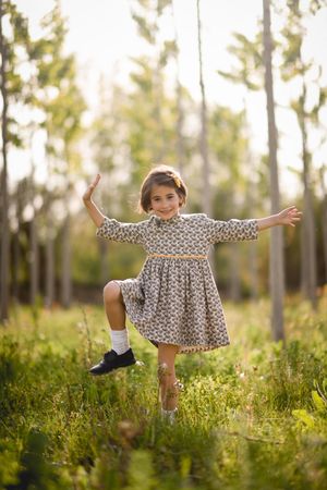 Happy child standing in dress in field surrounded by trees with open arms