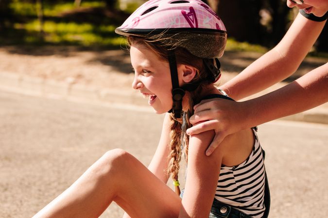Girl sitting on street wearing a protective helmet with a boy pushing her from behind