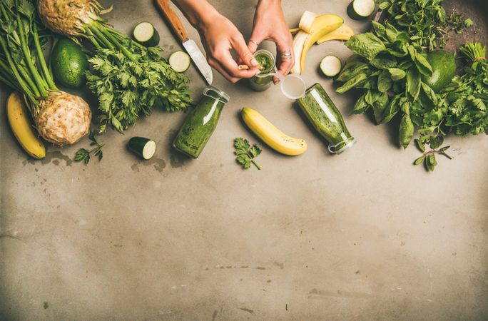 Green smoothie ingredients laying on grey background, with woman with holding smoothie, copy space