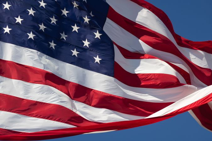 American Flag Waving In The Wind Against Deep Blue Sky.