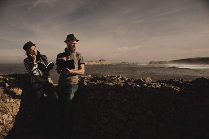 Man near woman with books near stones on shore
