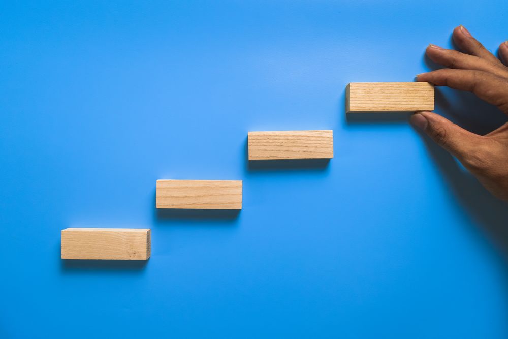 male hand put stairway wooden blocks isolated on blue background