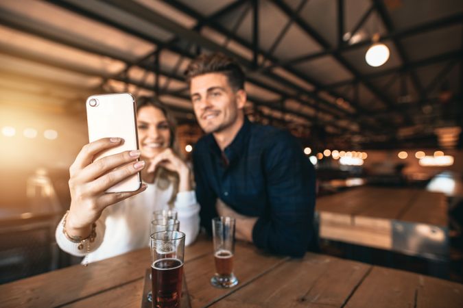 Smiling woman and man posing for selfie while enjoying craft beers at brewery