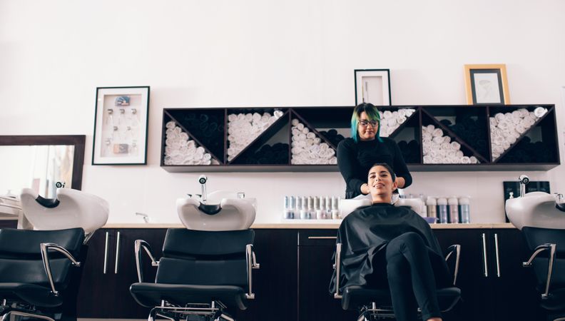 Woman sitting in salon chair while hairstylist towel dries her hair