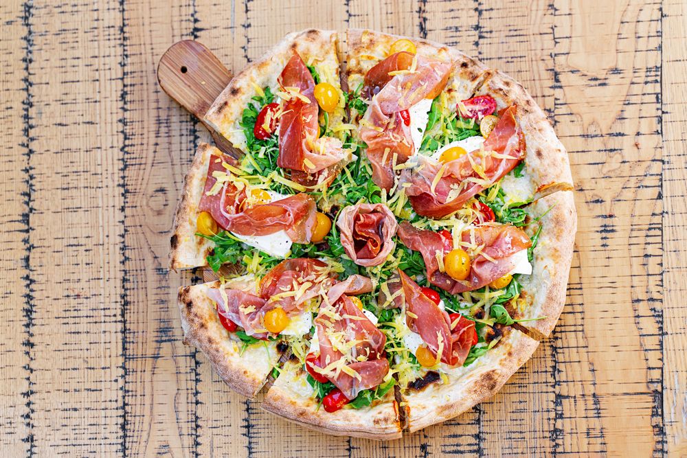 Gourmet Italian Pizza with Prosciutto, Arugula, and Colorful Cherry Tomatoes on Rustic Wooden Board