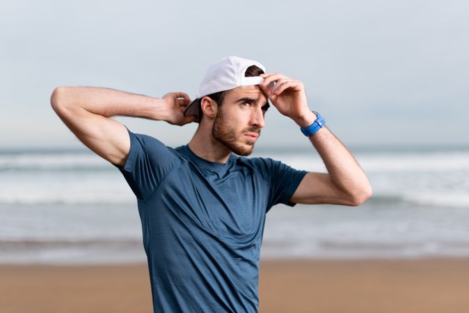 Confident male gymnast in active wear and cap on beach