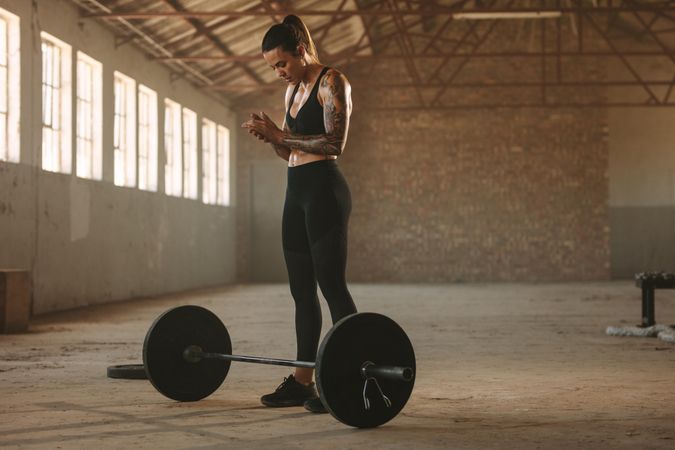 Strong female athlete standing with barbell on floor