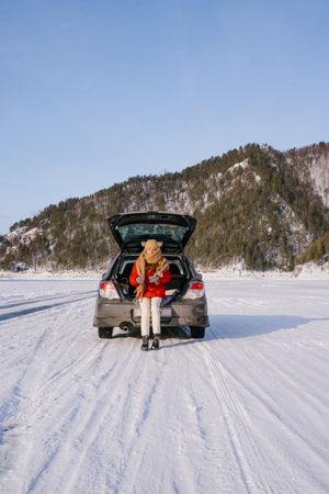 Woman sitting on car trunk in snowy valley