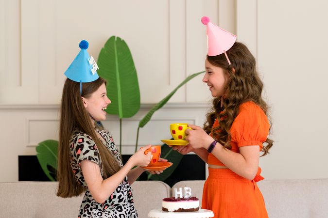 Two girls in birthday hats sharing joyful moment with tea