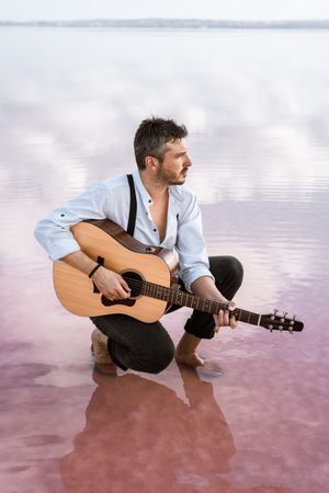 Musician with guitar on pink sandy water