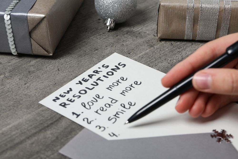 Gift boxes, paper with list and pen in hand on gray wooden background, close up