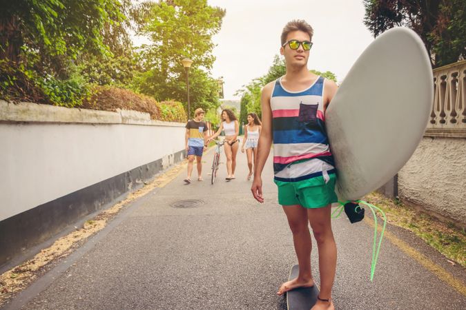Young man riding on skate and holding surfboard