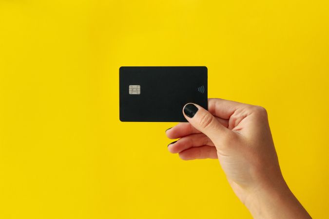 Female hand hold dark card on yellow background