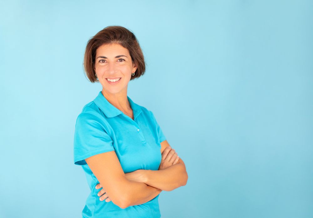 A woman, a physiotherapist, poses with a confident gesture, looking at the camera on a blue background, wearing a blue T-shirt