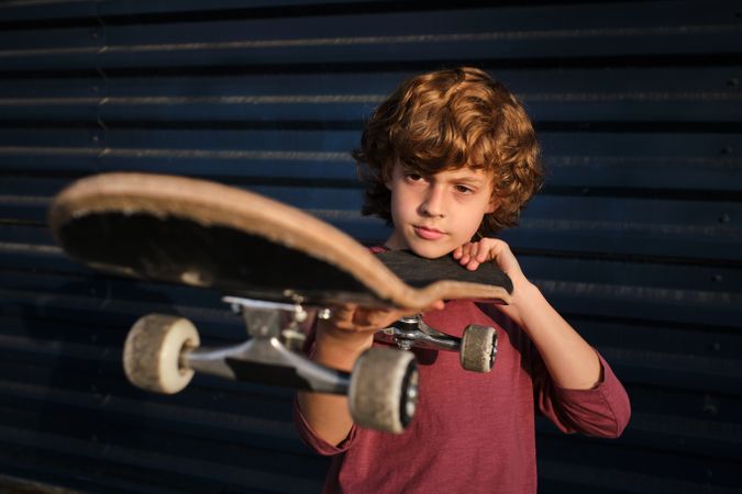 Little skater examining skateboard against wall