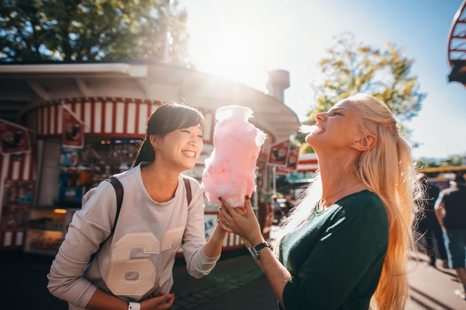 Shot of happy female friends in amusement park eating cotton candy