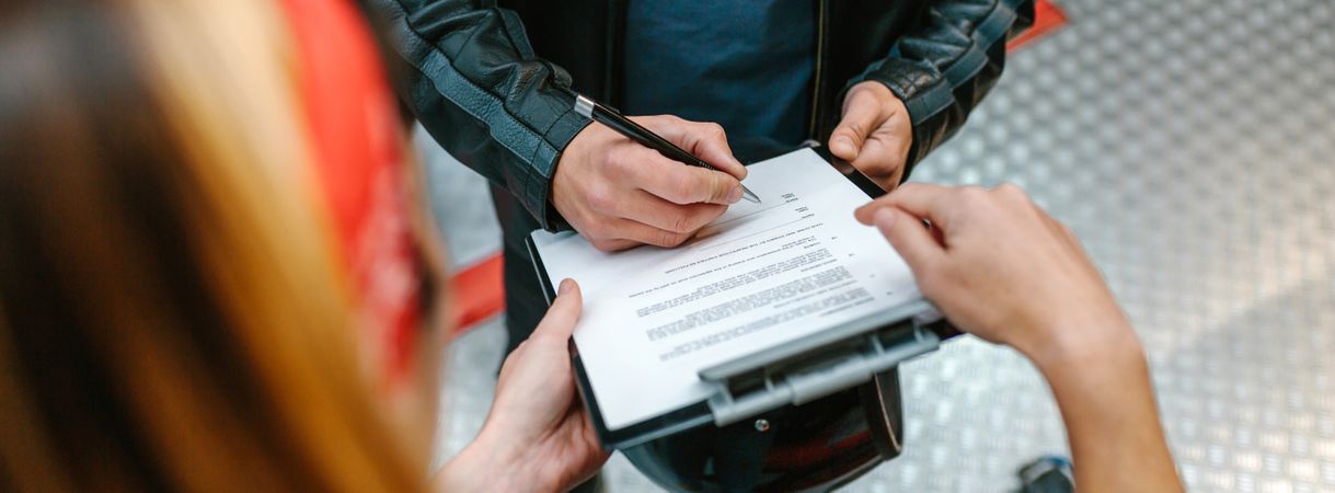 Female mechanic holding clipboard while biker man signing insurance policy on workshop