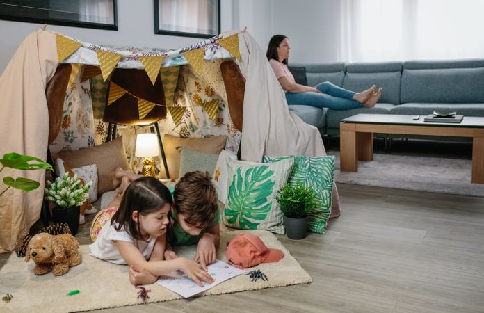 Children playing camping at home while their mother watches TV