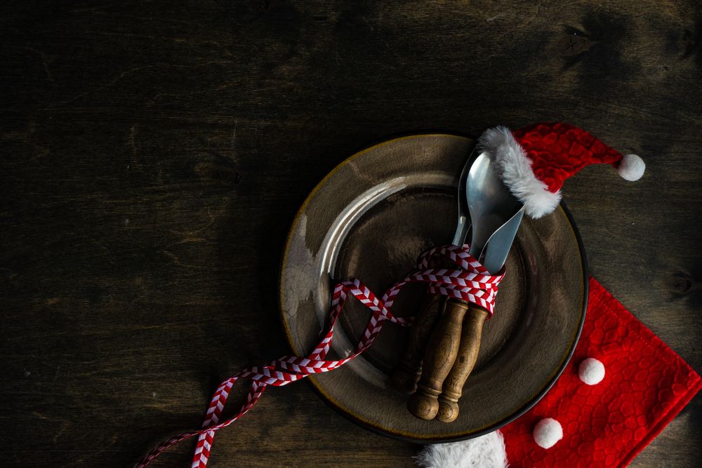 Cutlery setting with red Santa hat on silverware on brown plate rustic background