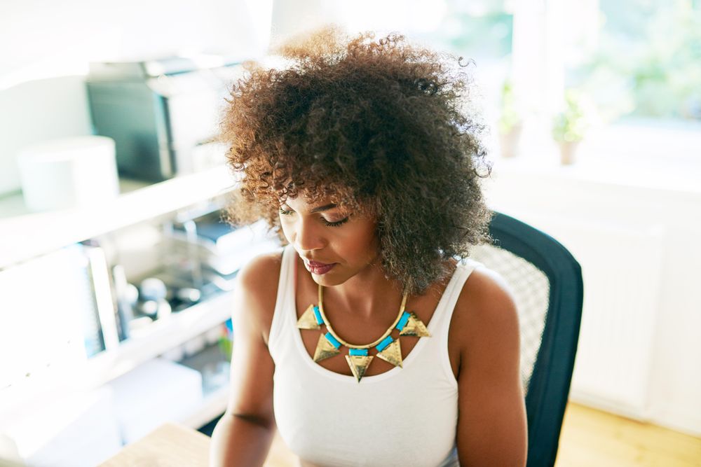 Black female looking down at her keyboard in bright home office