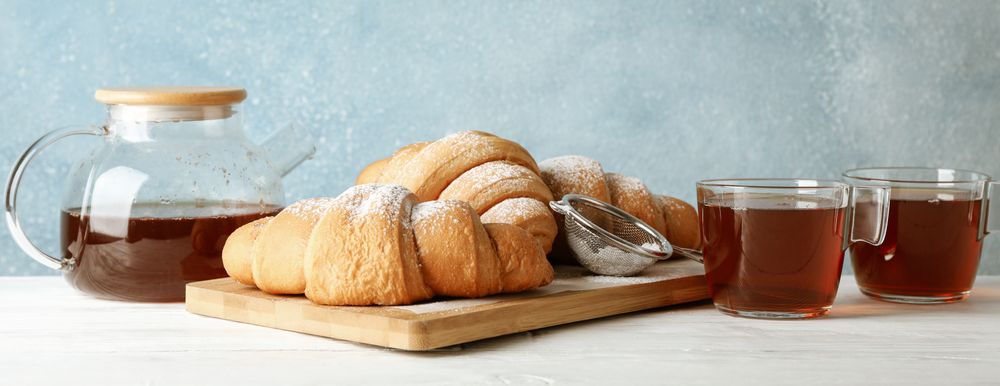 Tasty croissants and cups with tea on table, copy space