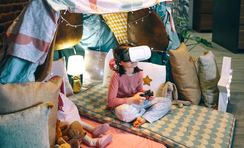 Digital native child looking metaverse world through VR glasses sitting over mats in a tent