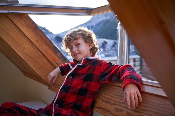 Boy leaning on opened window and looking at camera