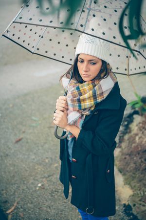 Woman contemplating while walking with umbrella on rainy day