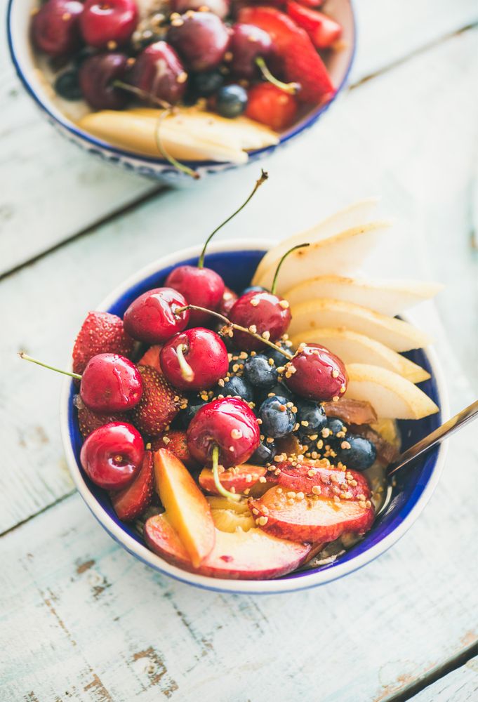 Top view of blue bowls of fresh fruit with cherries, peaches, blueberry